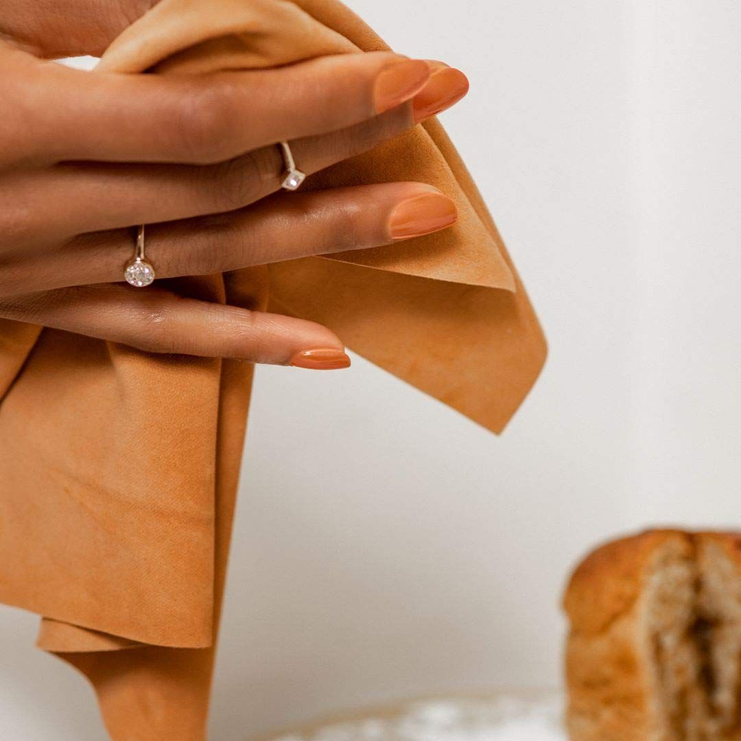 Hand mit lackierten, orangefarbenen Nägeln. Hält ein Tuch. Hintergrund: Brot.