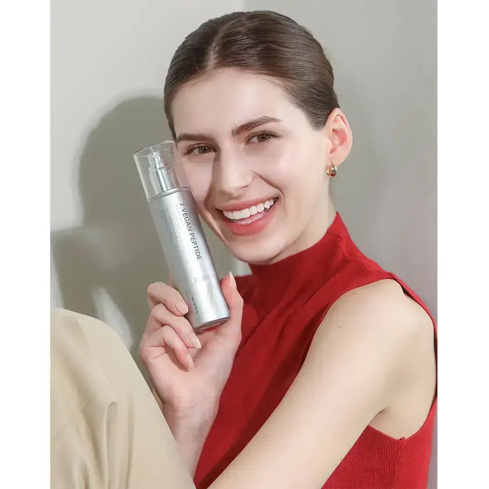 Frau hält eine silberne Flasche. Auf der Flasche steht "7 Vegan Peptide". Die Frau lächelt. Sie trägt ein rotes Oberteil und beigefarbene Hose.