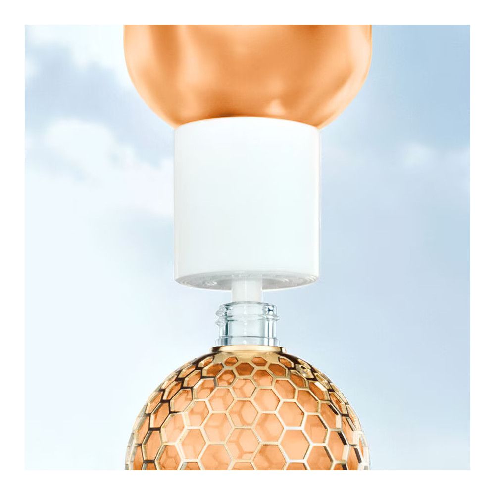 Flakon mit goldfarbenem Inhalt. Weißer Verschluss. Goldfarbenes Wabenmuster. Glasflakon.