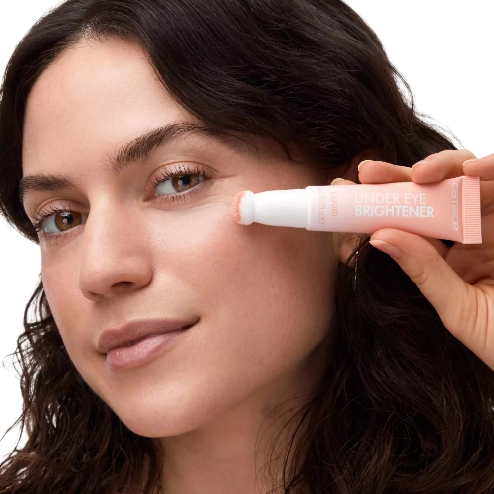 Frau hält rosa Tube mit weißem Applikator. Aufschrift: Under Eye Brightener. Keine Beschriftung sichtbar.