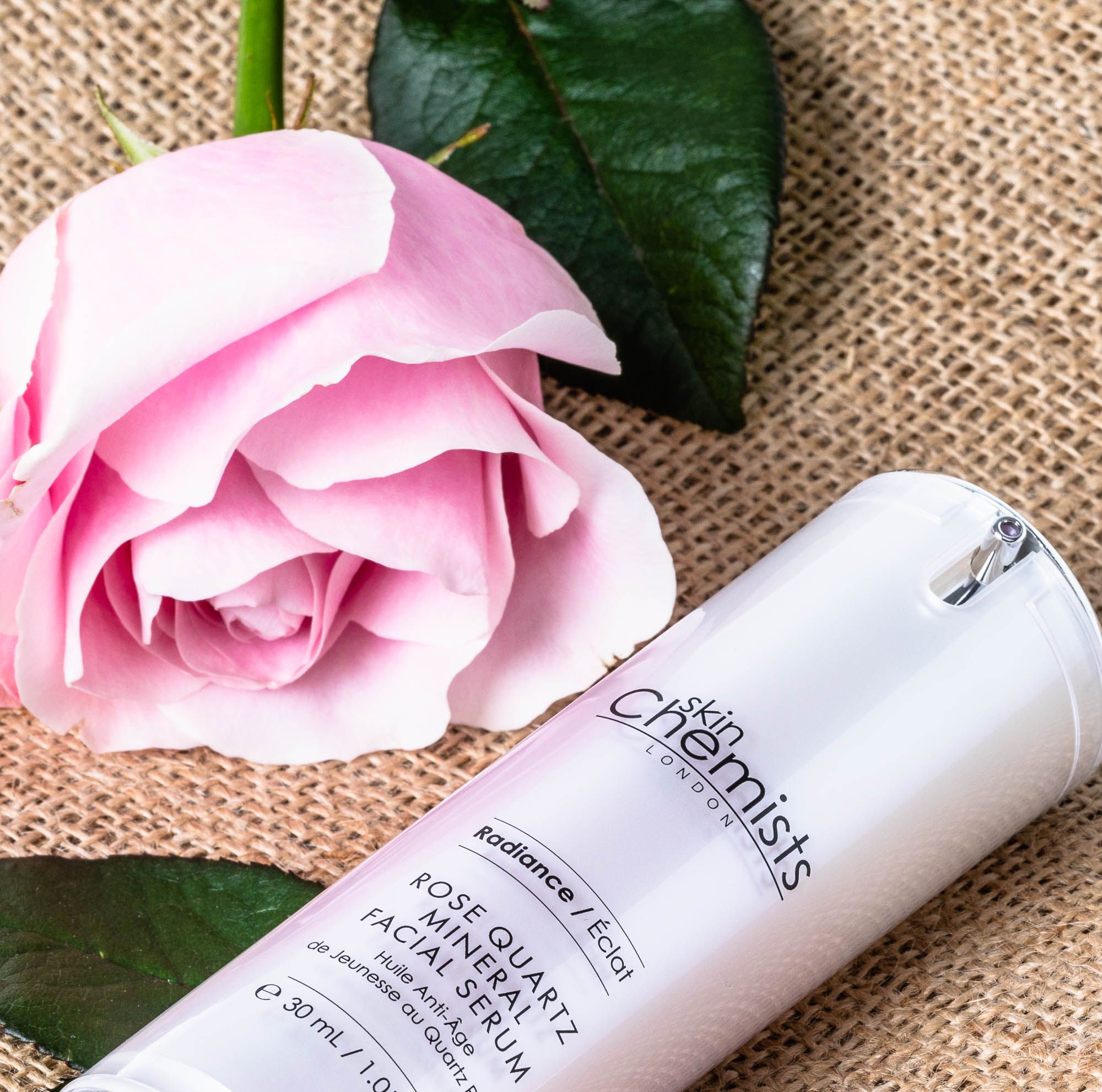 Produkt neben Rose und Blättern. Text: Rose Quartz Mineral Facial Serum, 30 ml. Flasche mit Pumpe.