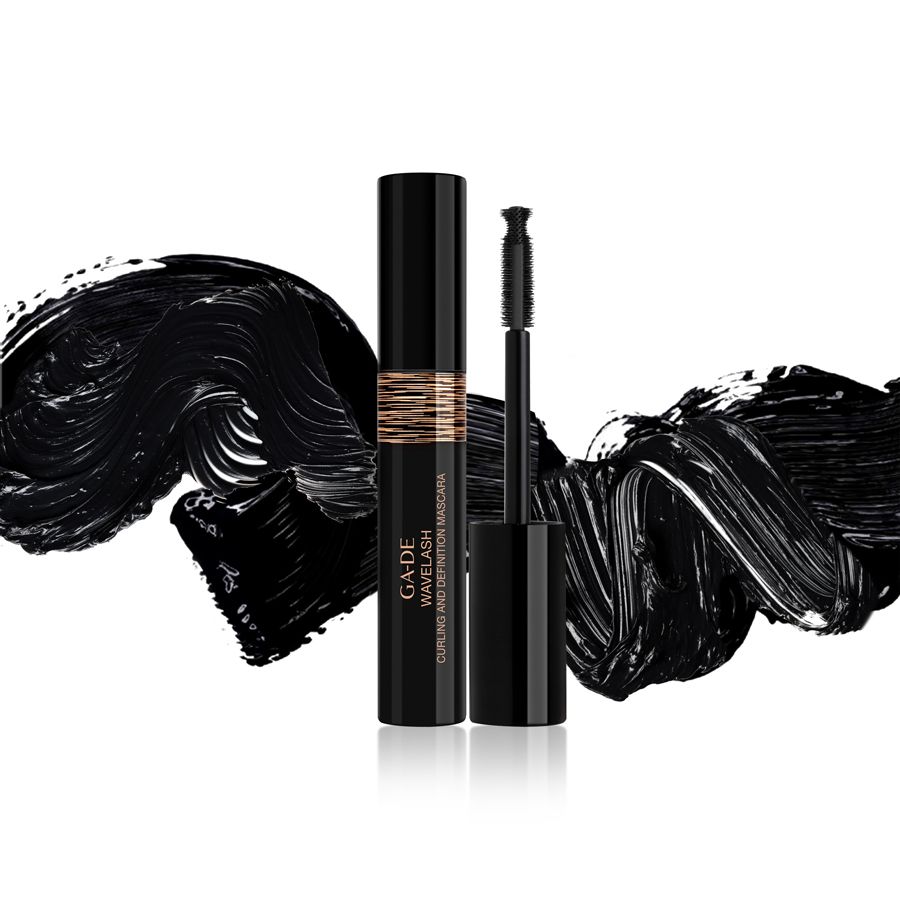 Schwarze Mascara-Tube und Bürste. Goldfarbener Streifen mit Schriftzug. Schwarze Mascara-Spuren im Hintergrund.
