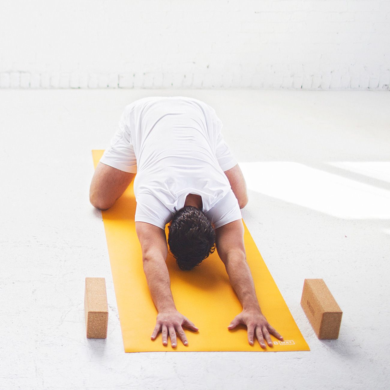 Person in Yoga-Position auf gelber Yogamatte. Zwei Holzblöcke liegen daneben.