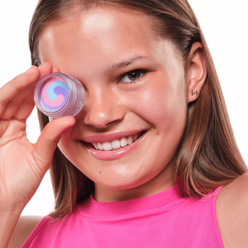 Ein Mädchen hält einen Tiegel vor einem Auge. Der Tiegel enthält eine Lippenmaske. Schriftzug: essence LIP swirl caring mask.