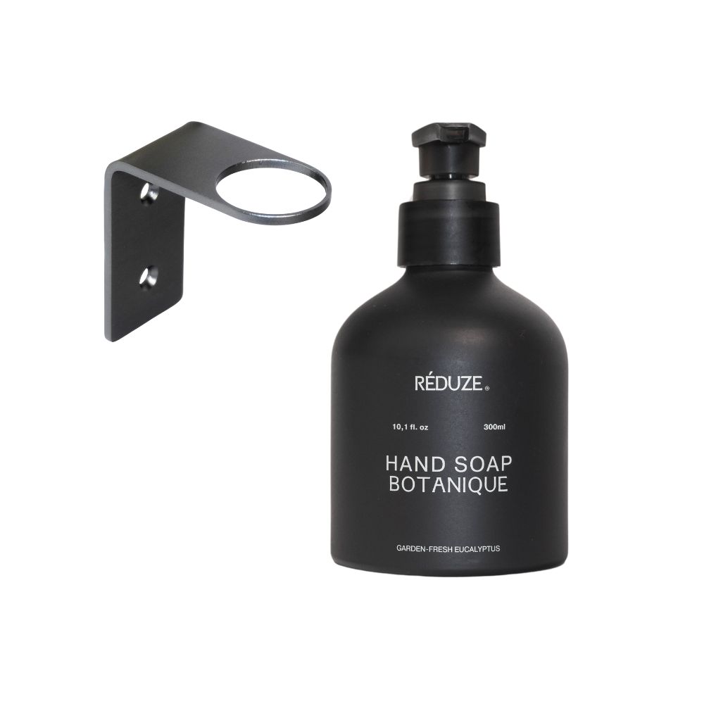 Schwarze Handseife mit Wandhalterung. Aufschrift: HAND SOAP BOTANIQUE. Schwarzer Spender mit Pumpkopf. Wandhalterung aus Metall.