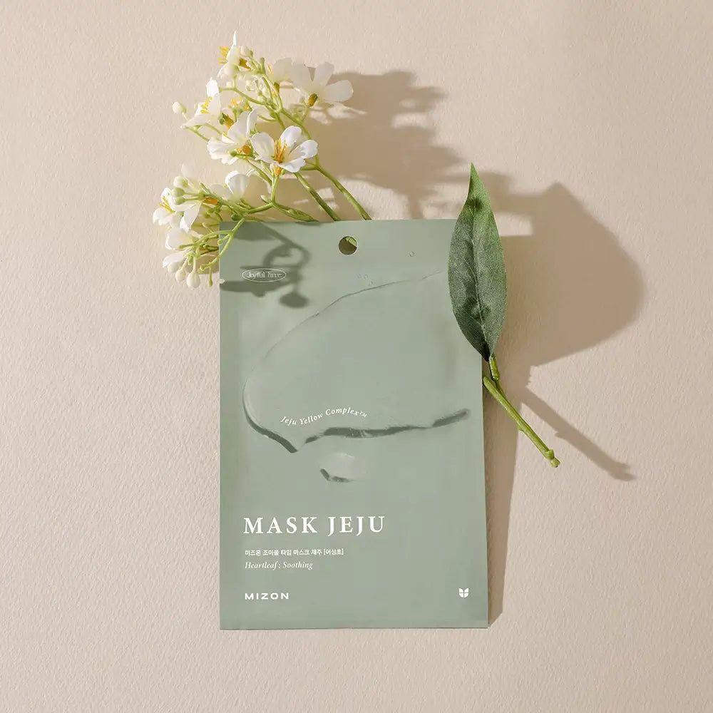 Grüne Produktverpackung mit Blume und Blatt. Text: MASK JEJU, MIZON. Auf hellem Hintergrund.