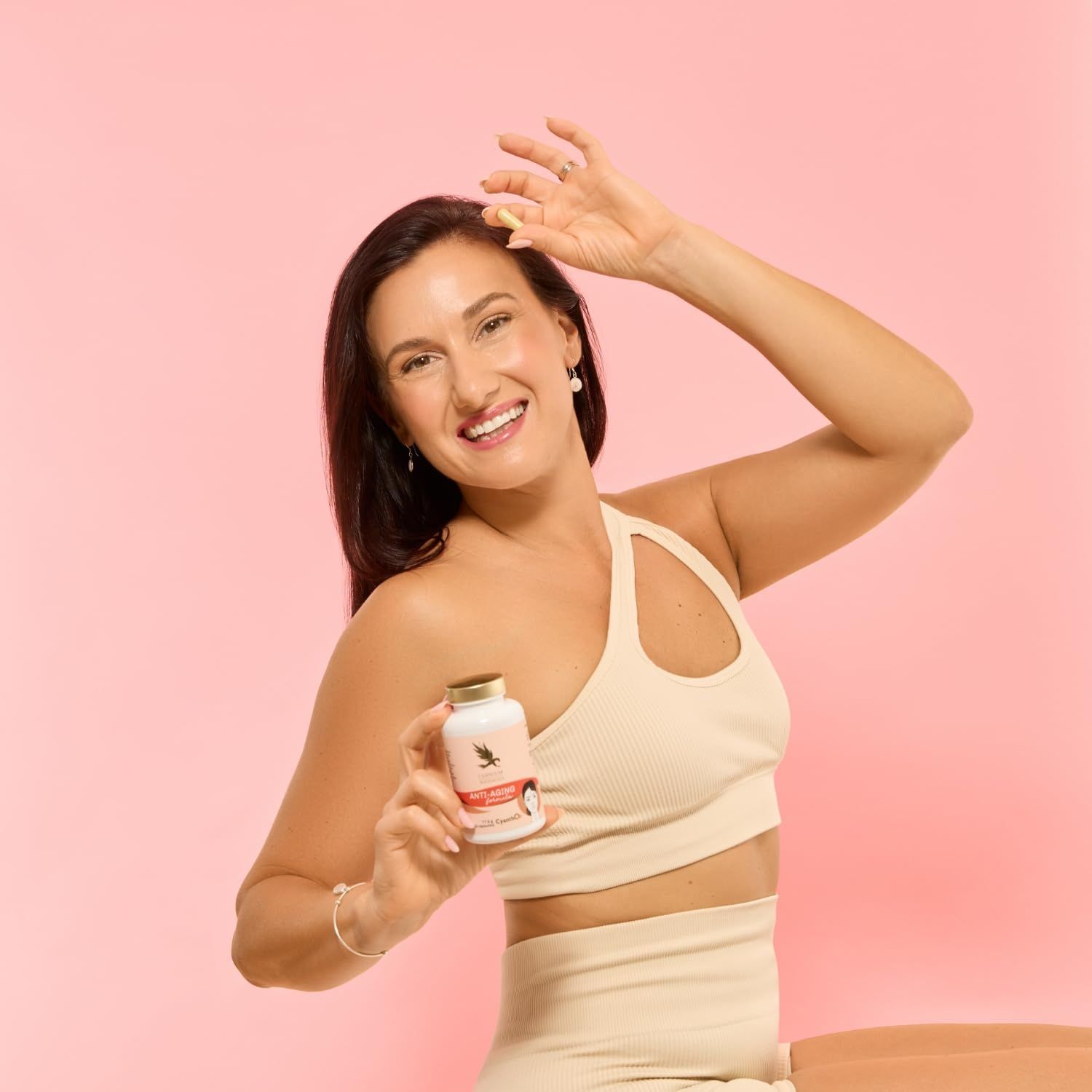 Frau hält Pillenfläschchen mit goldenem Deckel. Aufschrift: Anti-Aging formula. Frau lächelt.