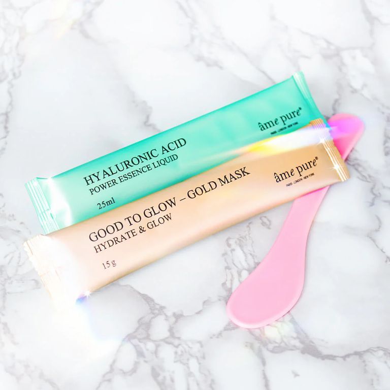 Zwei Maskenbeutel und ein Spatel. Grün und Gold. Text: âme pure, Hyaluronic Acid, Good to Glow. Auf weißem Marmor.