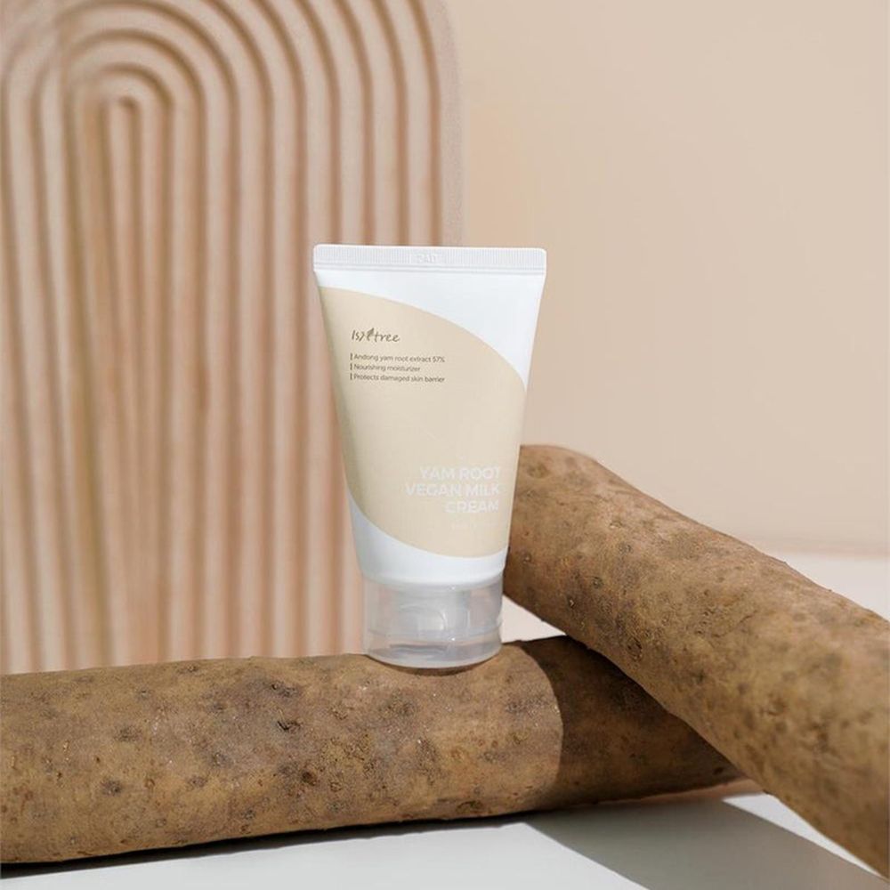 Creme-Tube vor Yamswurzeln. Aufschrift: YAM ROOT VEGAN MILK CREAM. Marke: ISNTREE. Hintergrund: beige Bögen. Transparenter Verschluss.