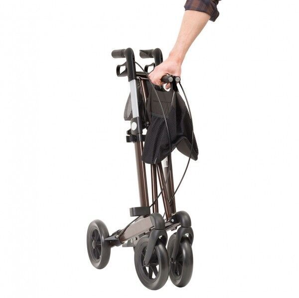 Rollator, braun, zusammengeklappt. Schwarze Tasche, Handgriff. Person hält den Rollator.