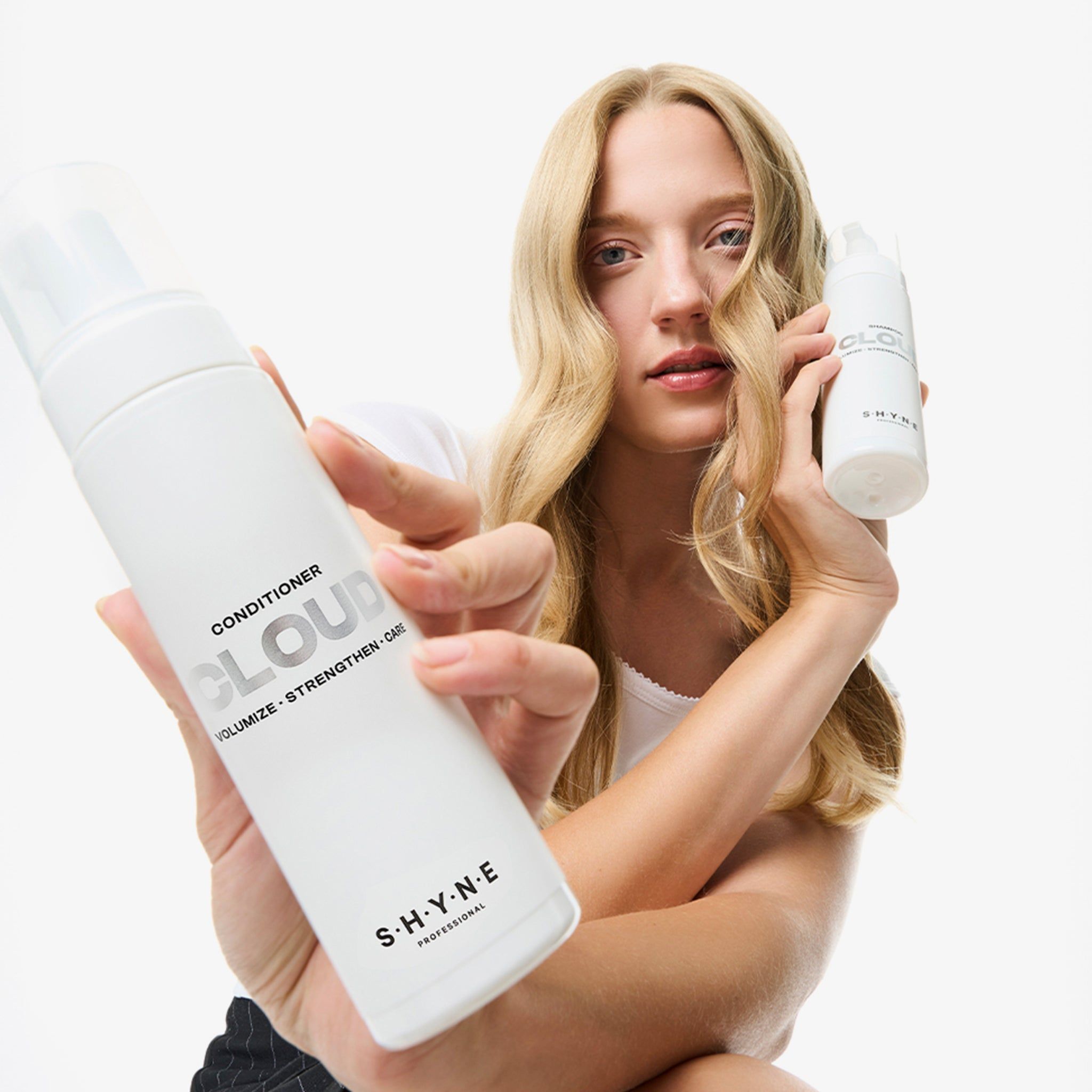 Frau hält zwei weiße Flaschen. Auf einer steht "CONDITIONER CLOUD" und "S.H.Y.N.E".