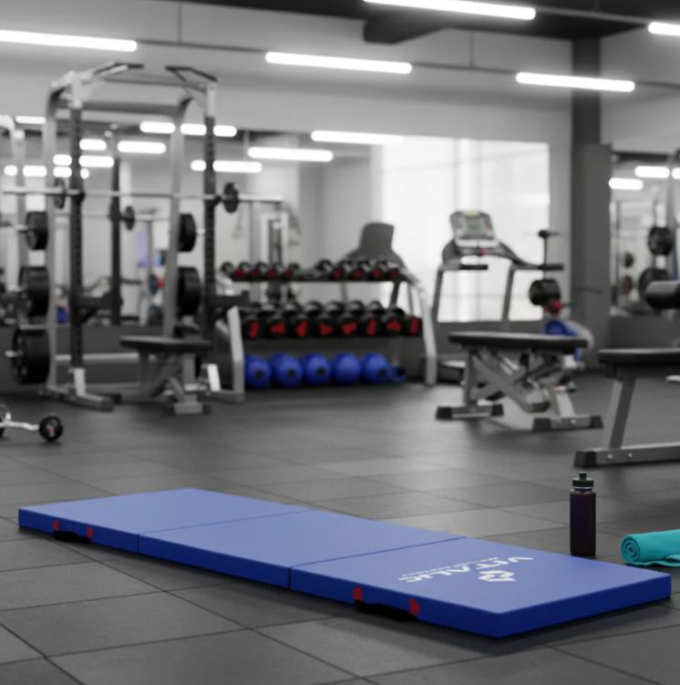 Blaue Fitnessmatte in einem Fitnessstudio. Weitere Sportgeräte im Hintergrund.