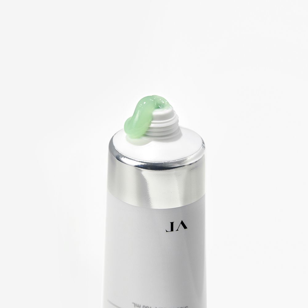 Nahaufnahme einer Tube. Weiße Tube mit silbernem Deckel, grüne Creme tritt aus der Öffnung aus.