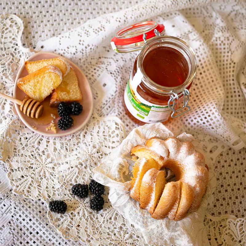 Honigglas mit Etikett, geöffnet. Kuchen, Beeren und Honig auf Teller mit Honiglöffel.