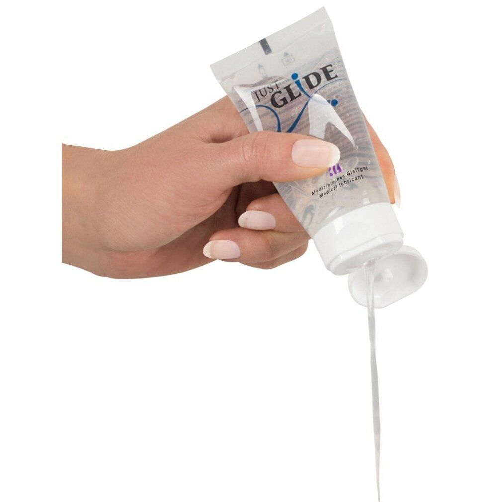 Hand hält eine Tube, aus der transparentes Gel fließt. Aufschrift: JUST GLIDE, TOYS, Medizinischer Gleitgel, Medical lubricant.
