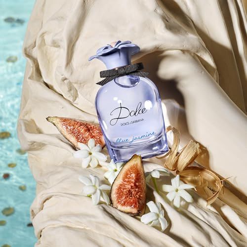 Hellblaues Parfümflakon mit schwarzer Schleife und hellblauer Blüte, neben Feigen und Jasminblüten auf einer Statue.