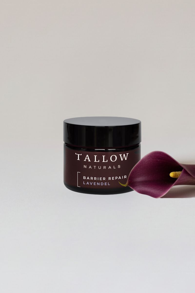 Braunes Tiegel mit schwarzem Deckel. Aufschrift: TALLOW NATURALS, BARRIER REPAIR LAVENDEL. Daneben eine dunkelviolette Calla-Blüte.