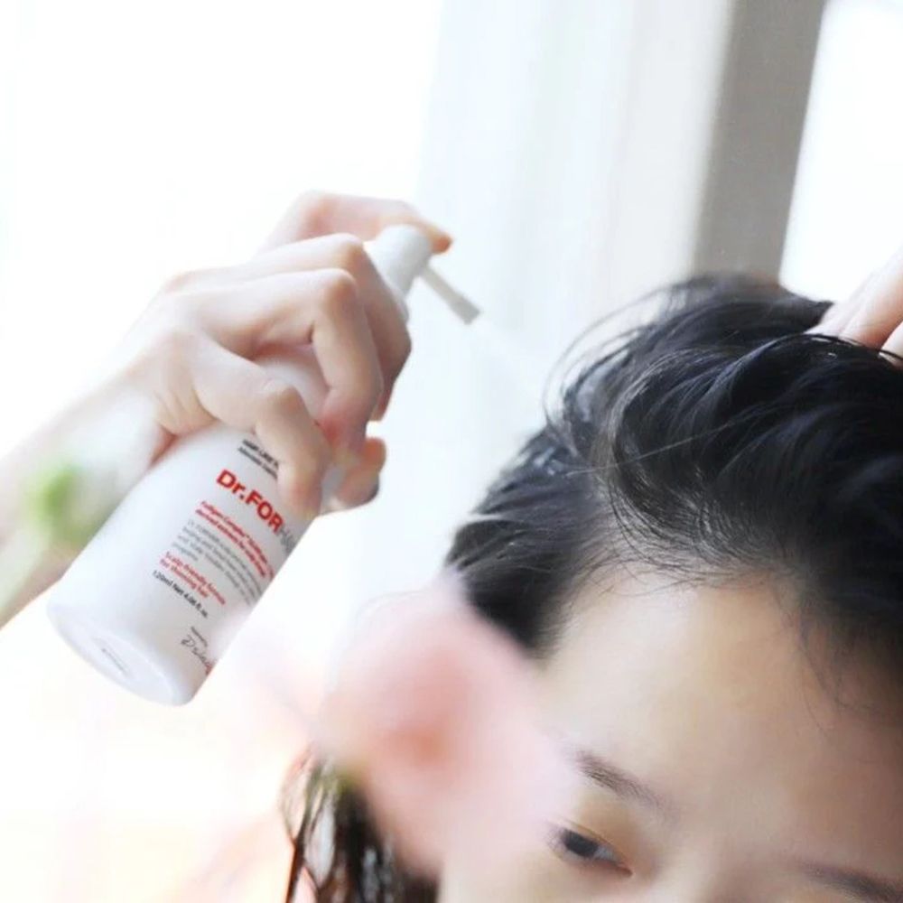 Hand sprüht Dr. FORHAIR Folligen Scalp Tonic auf die Kopfhaut.