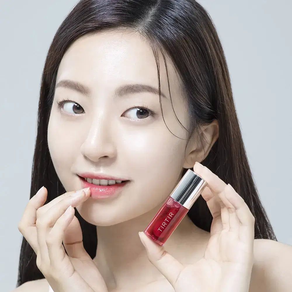 Frau hält Lip Oil. Das Produkt ist rot und hat einen silbernen Deckel. Die Frau berührt ihre Lippen.