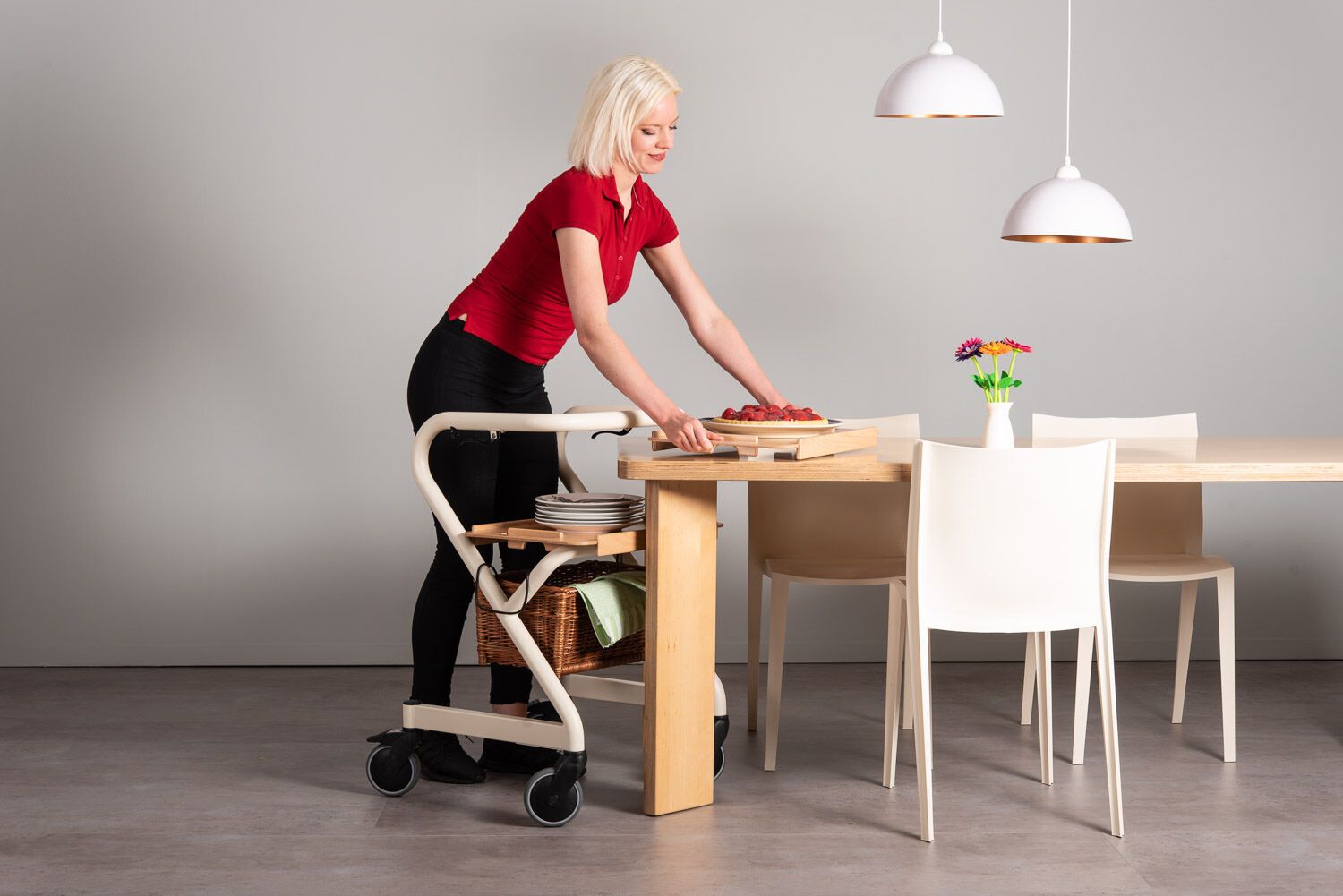 Person mit Rollator. Holztablett mit Essen. Rollator mit Korb. Frau in rotem Shirt.