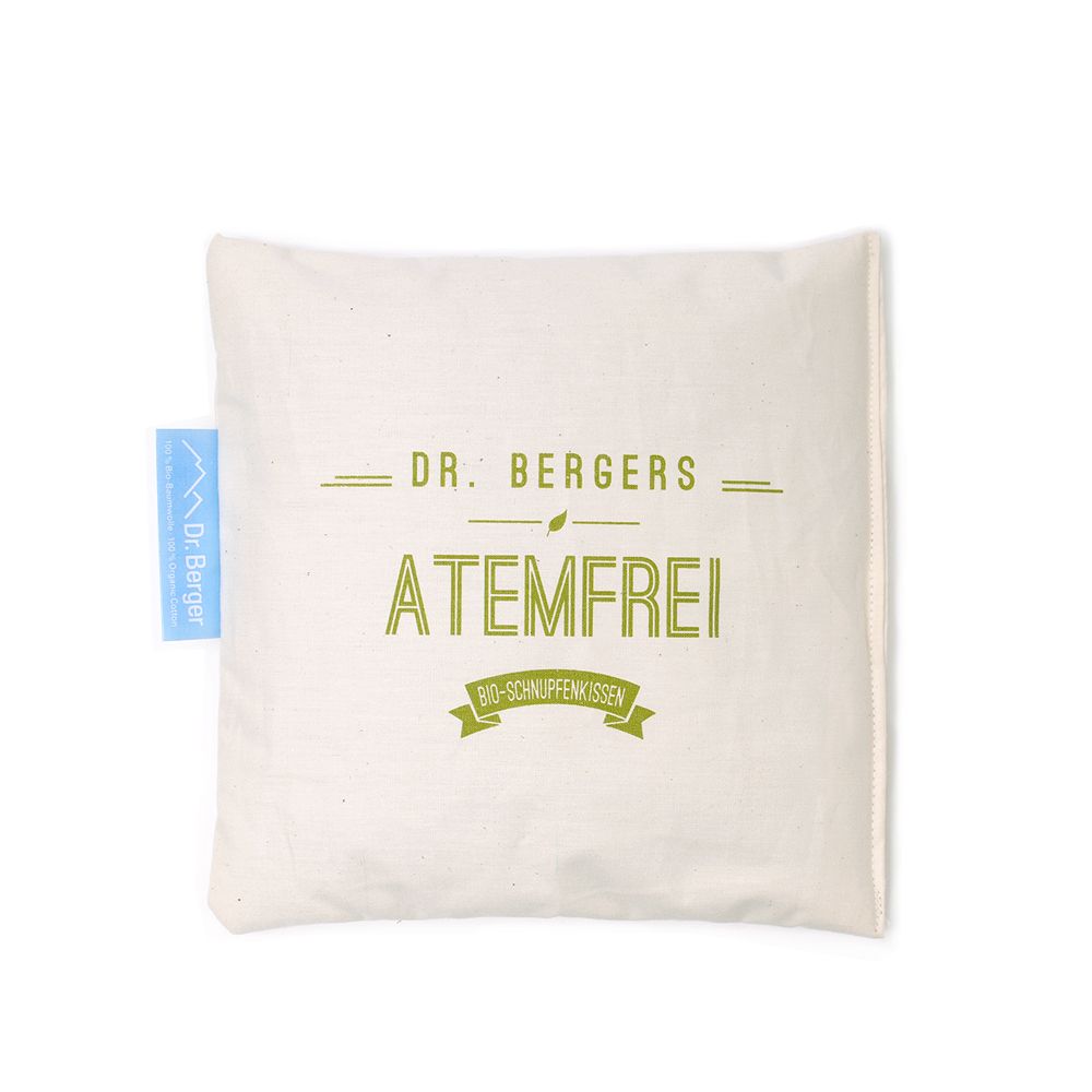 Quadratisches Kissen mit Aufdruck. Aufschrift: DR. BERGERS ATEMFREI. Kleines blaues Etikett mit Logo. Beige Stoff.