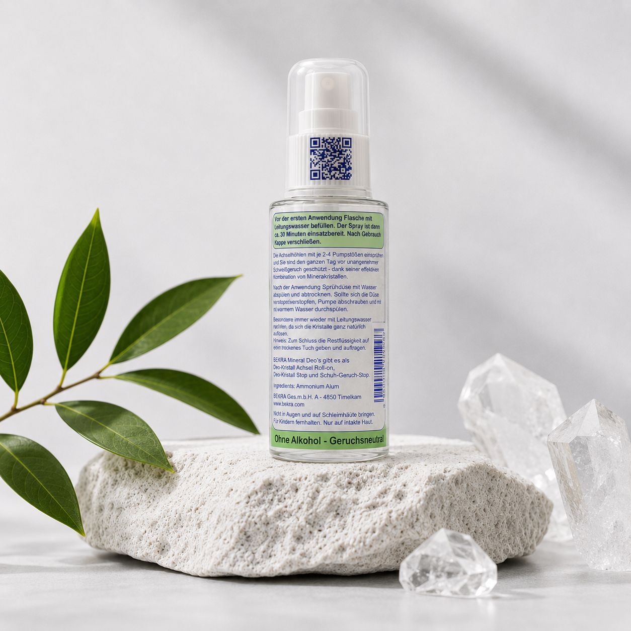 Rückseite des BEKRA Mineral Kristall Deo Spray mit QR-Code und Anwendungshinweisen. Auf Stein mit Blättern und Kristallen.