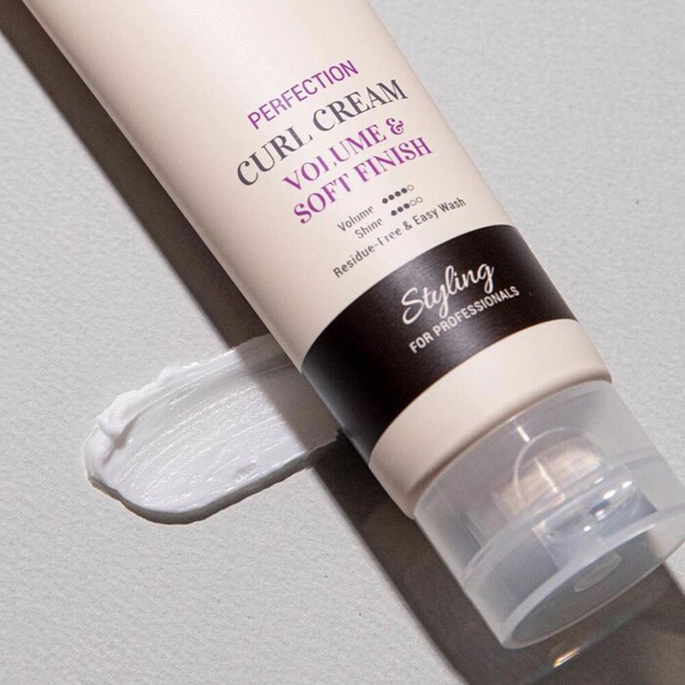 Nahaufnahme einer Creme-Tube und Creme-Ausstrich. Text: CURLY SHYLL, Perfection Curl Cream, Volume & Soft Finish. Styling-Logo.