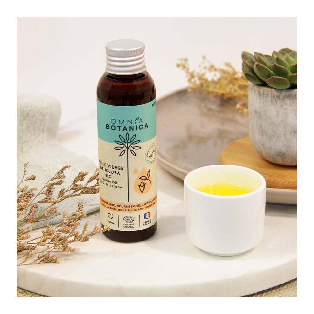 Braune Glasflasche mit silbernem Deckel. Etikett mit Produktbezeichnung und Logo. Neben einem weißen Becher mit gelber Flüssigkeit.