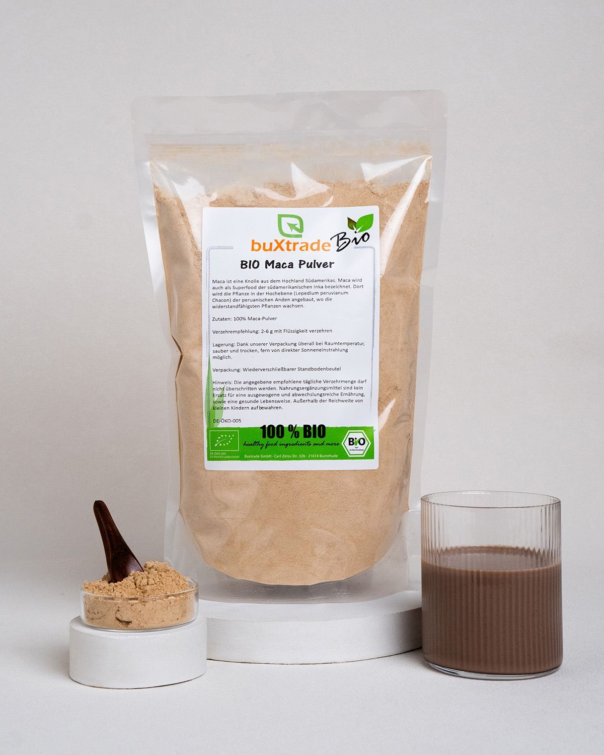 Beutel buXtrade Bio Maca Pulver, Glas mit Flüssigkeit, Löffel mit Pulver. Bio-Siegel. Helles Ambiente.
