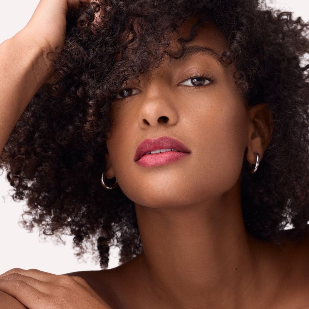 Porträt einer Frau mit Locken und rotem Lippenstift. Sie trägt Ohrringe.