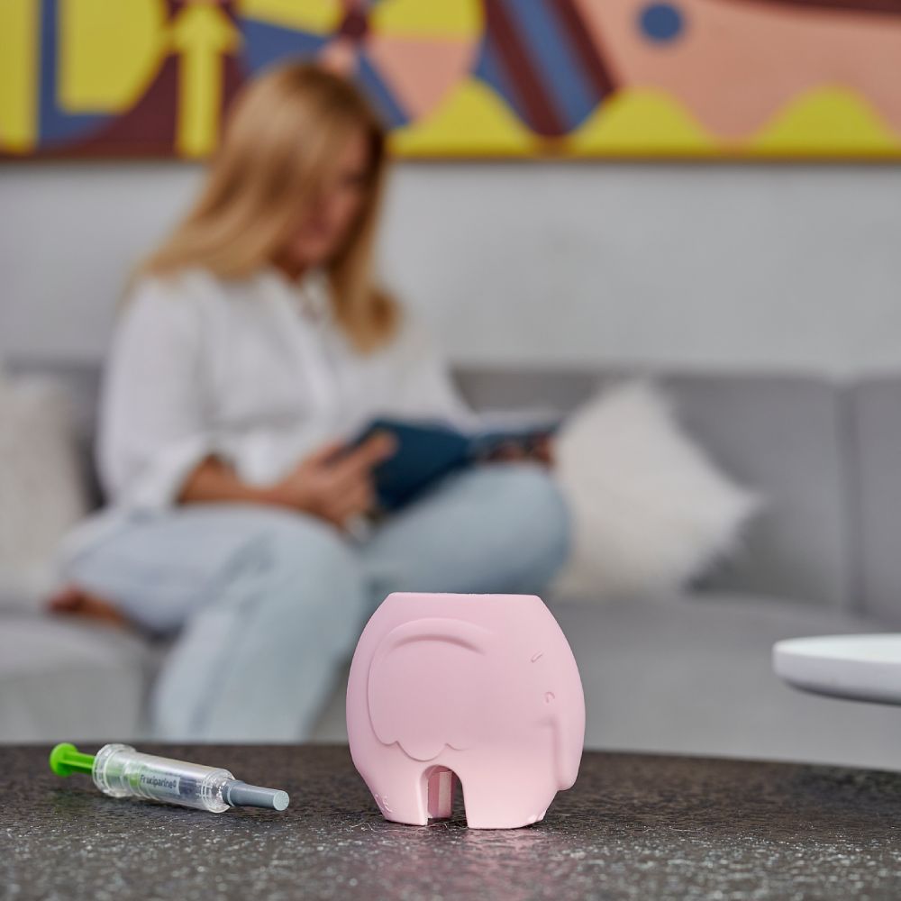 Rosa Spritzenhilfe in Elefantenform auf Tisch. Daneben Spritze mit grünem Kolben.