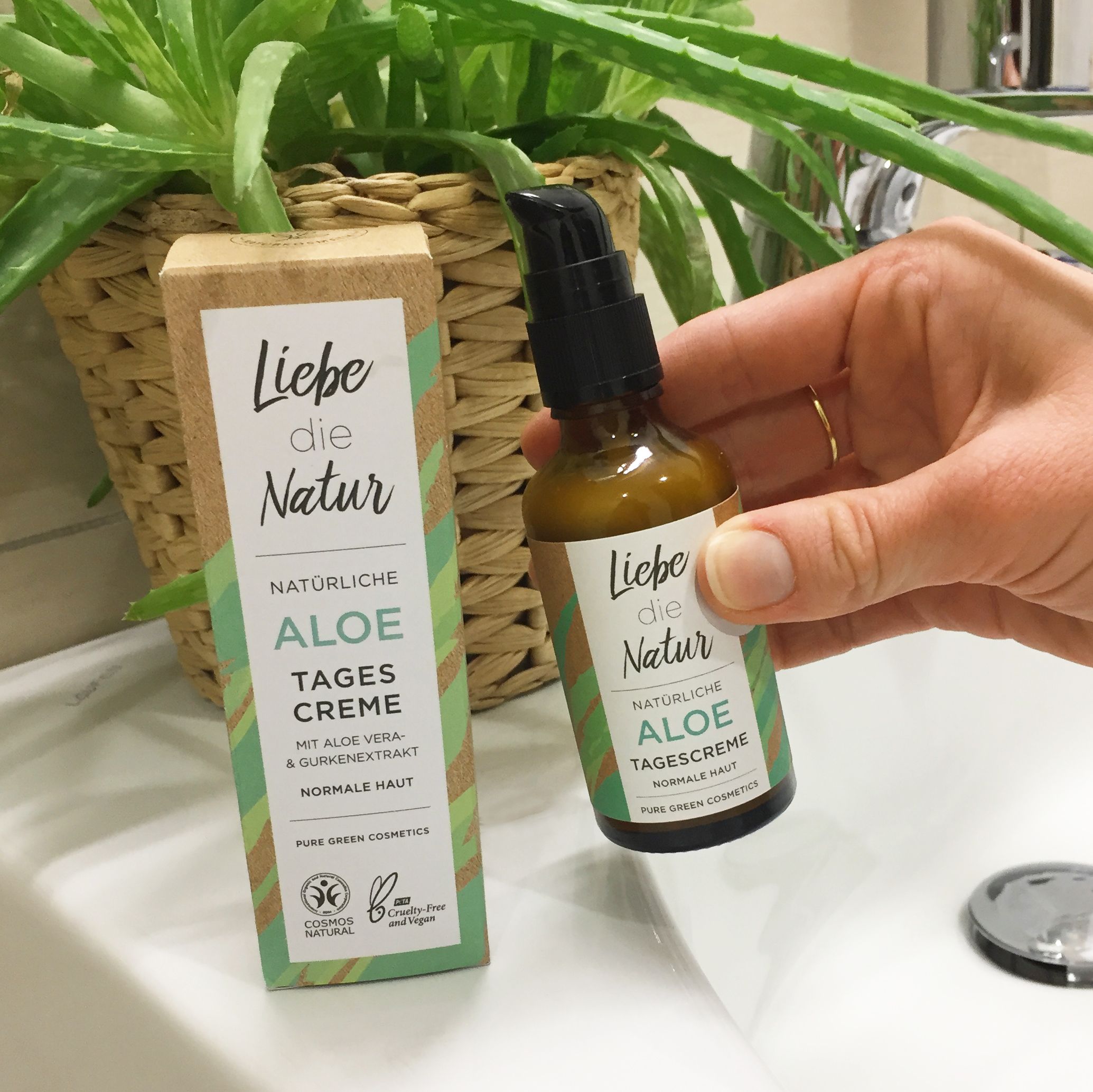 Braune Glasflasche mit Pumpe und Karton. Aufschrift: Aloe Tagescreme, normale Haut. Zertifizierungen.