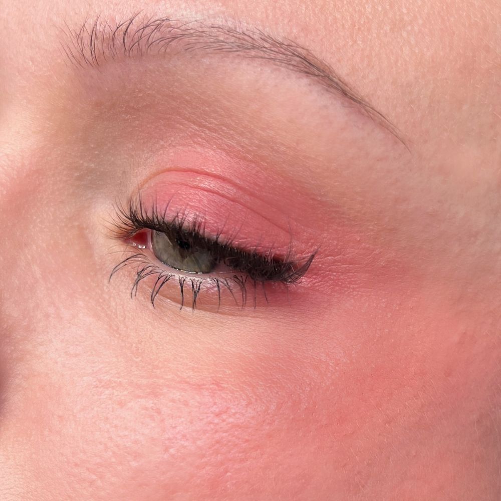 Nahaufnahme eines Auges mit rosa Lidschatten und Wimperntusche. Hautton.