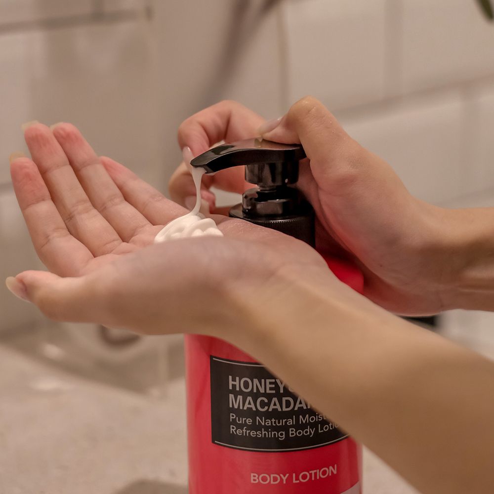 Hände drücken Lotion aus einer rosa Flasche. Schwarzer Pumpkopf. Text: Honey & Macadamia, Pure Natural Moisturizing Body Lotion.