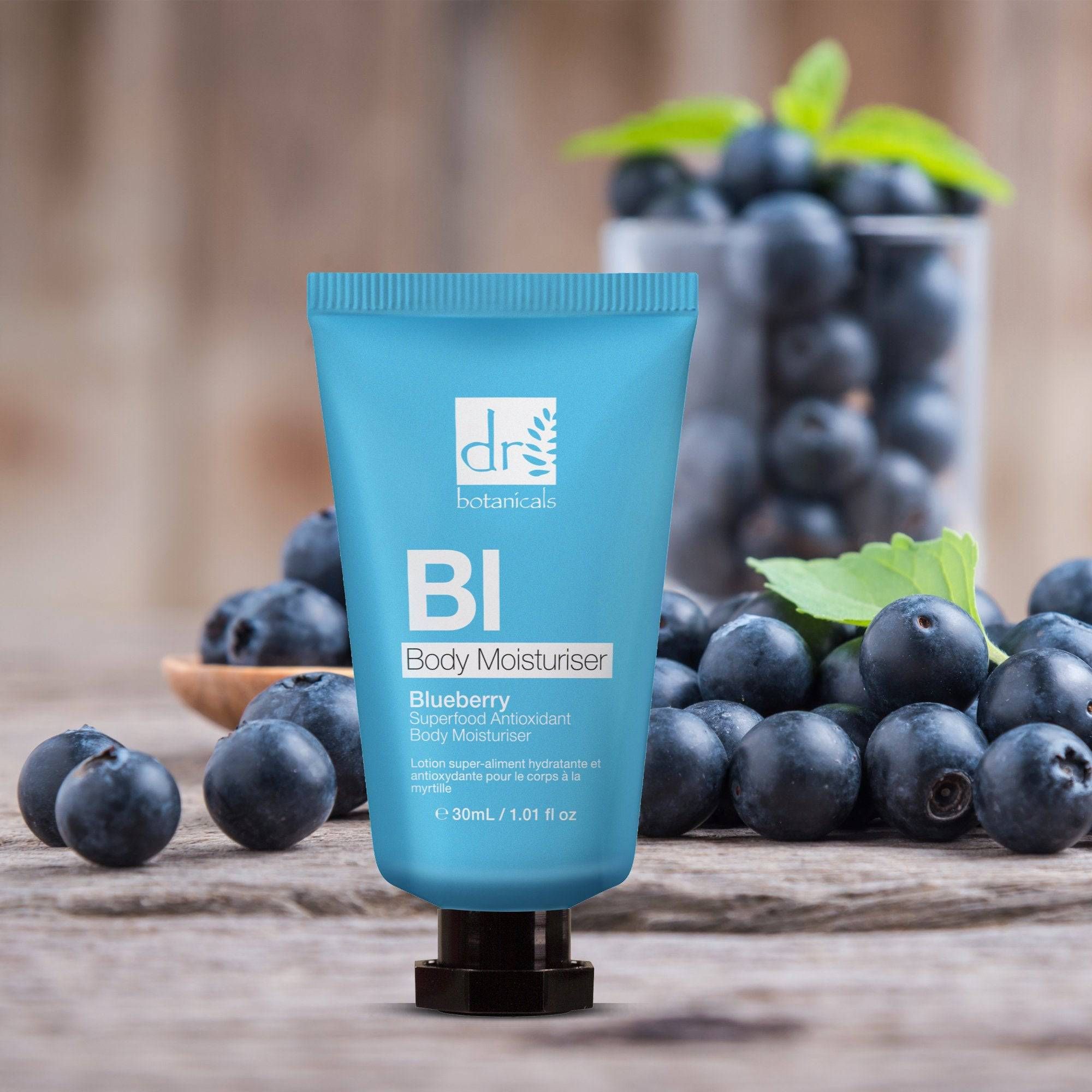 Blaue Tube auf Holzoberfläche mit Blaubeeren. Aufschrift: BI Body Moisturiser, Blueberry Superfood Antioxidant Body Moisturiser.