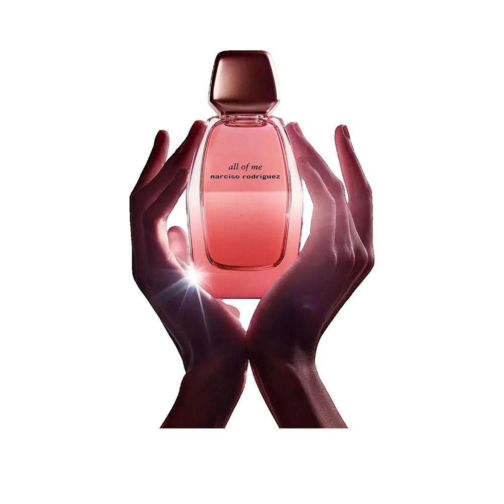 Parfümflakon, rosa Flüssigkeit, goldfarbener Verschluss. Hände halten Flakon. Aufschrift: all of me, narciso rodriguez.