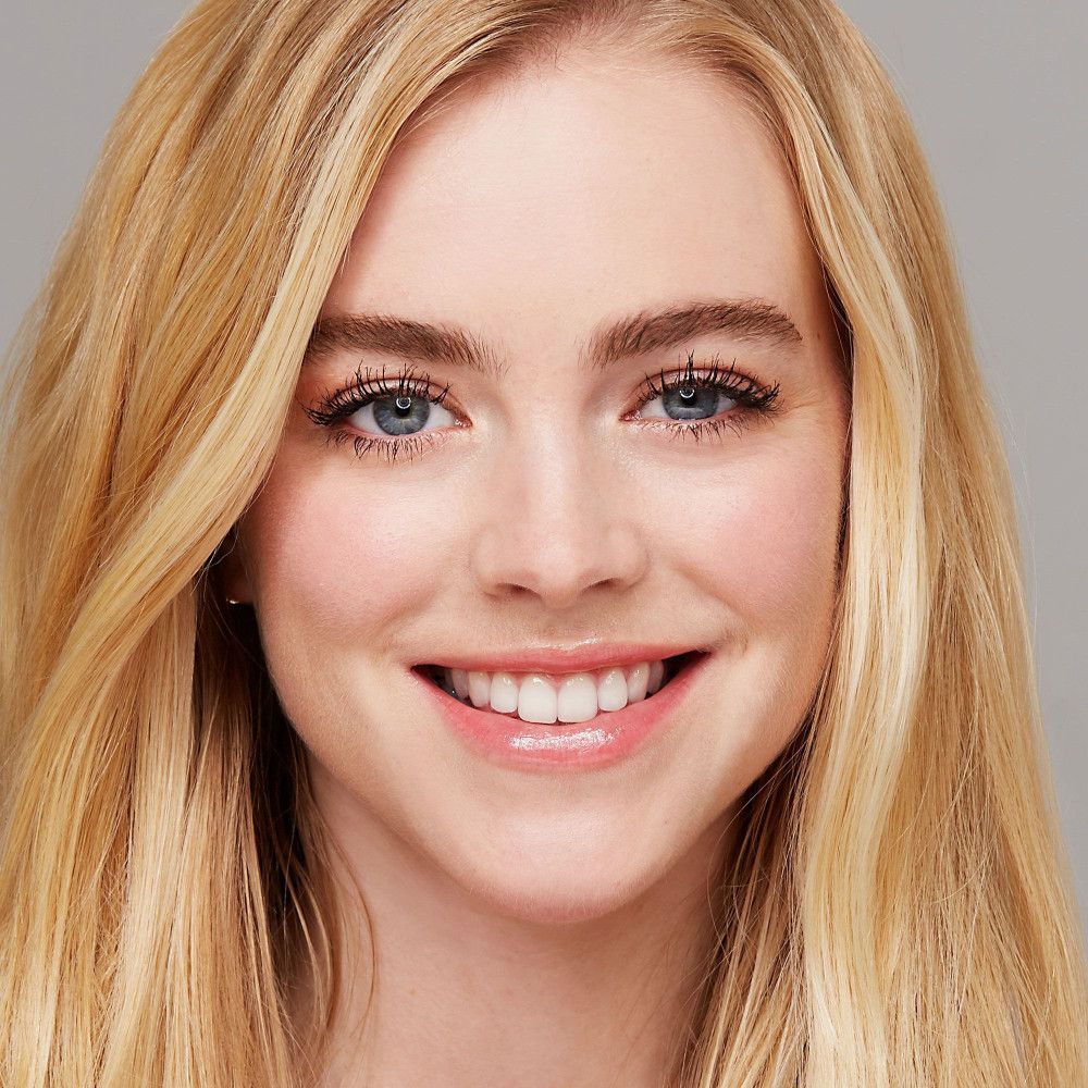 Porträt einer Frau mit blonden Haaren und getuschten Wimpern. Sie lächelt.