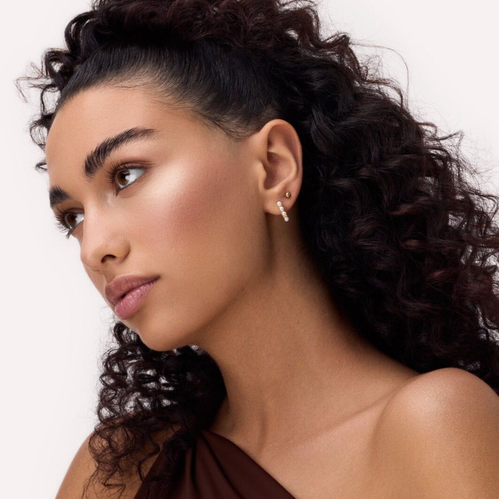 Porträt einer Frau mit Locken und aufgetragenem Highlighter. Hautton und Ohrringe sind sichtbar.