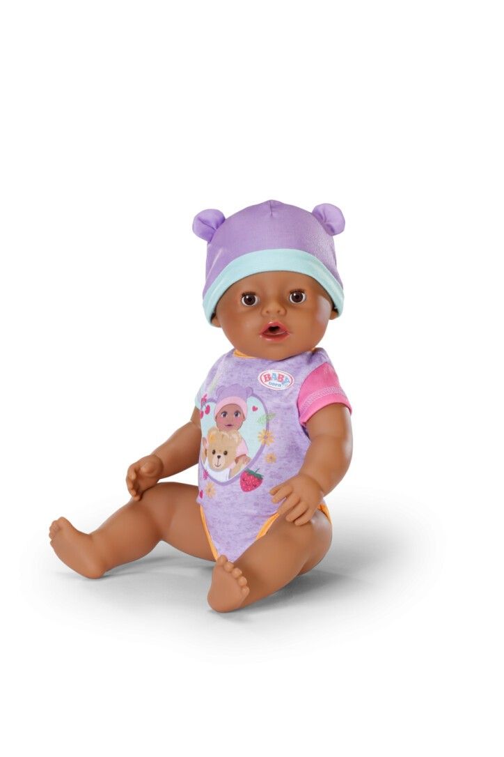 BABY born Puppe mit lila Mütze und Strampler. Puppe sitzt. Hautfarbe: braun.