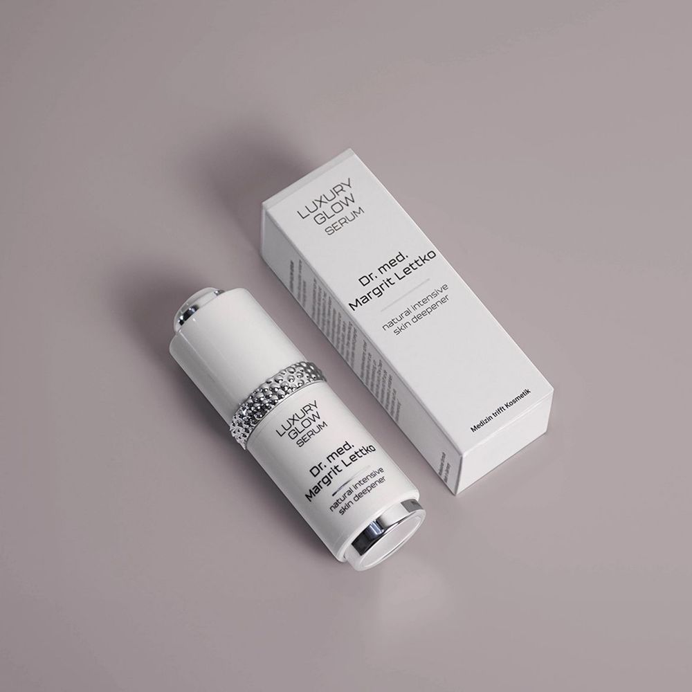 Dr. med. Margrit Lettko Luxury Glow Serum in weißer Spenderflasche mit silbernem Applikator und Umverpackung.