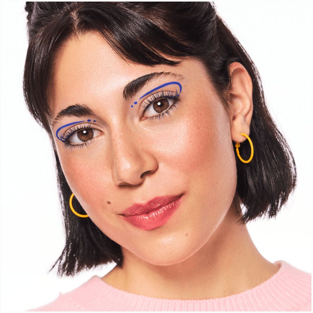 Frau mit blauem Eyeliner-Design um die Augen. Gelbe Ohrringe. Rosa Oberteil.