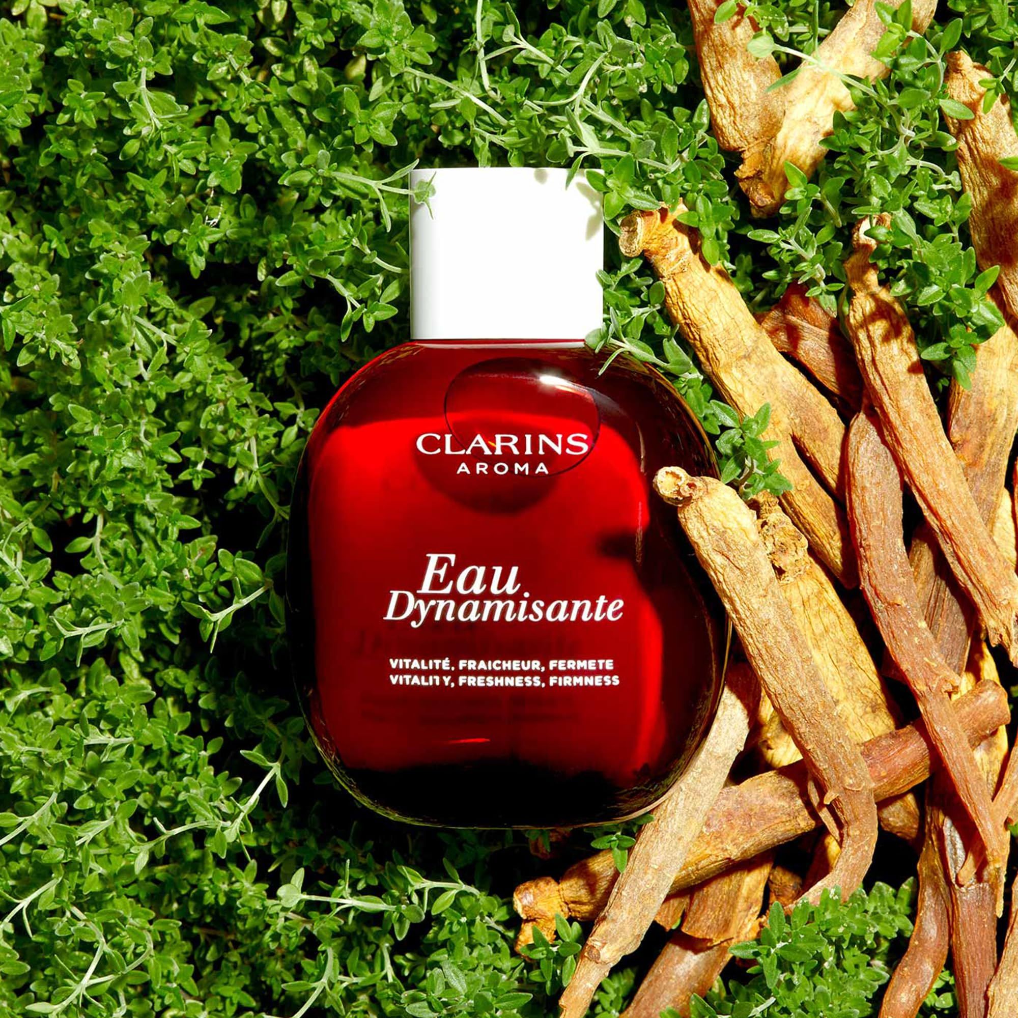 Rote Flasche mit weißem Verschluss, umgeben von Kräutern und Wurzeln. Aufschrift: Clarins Aroma, Eau Dynamisante.