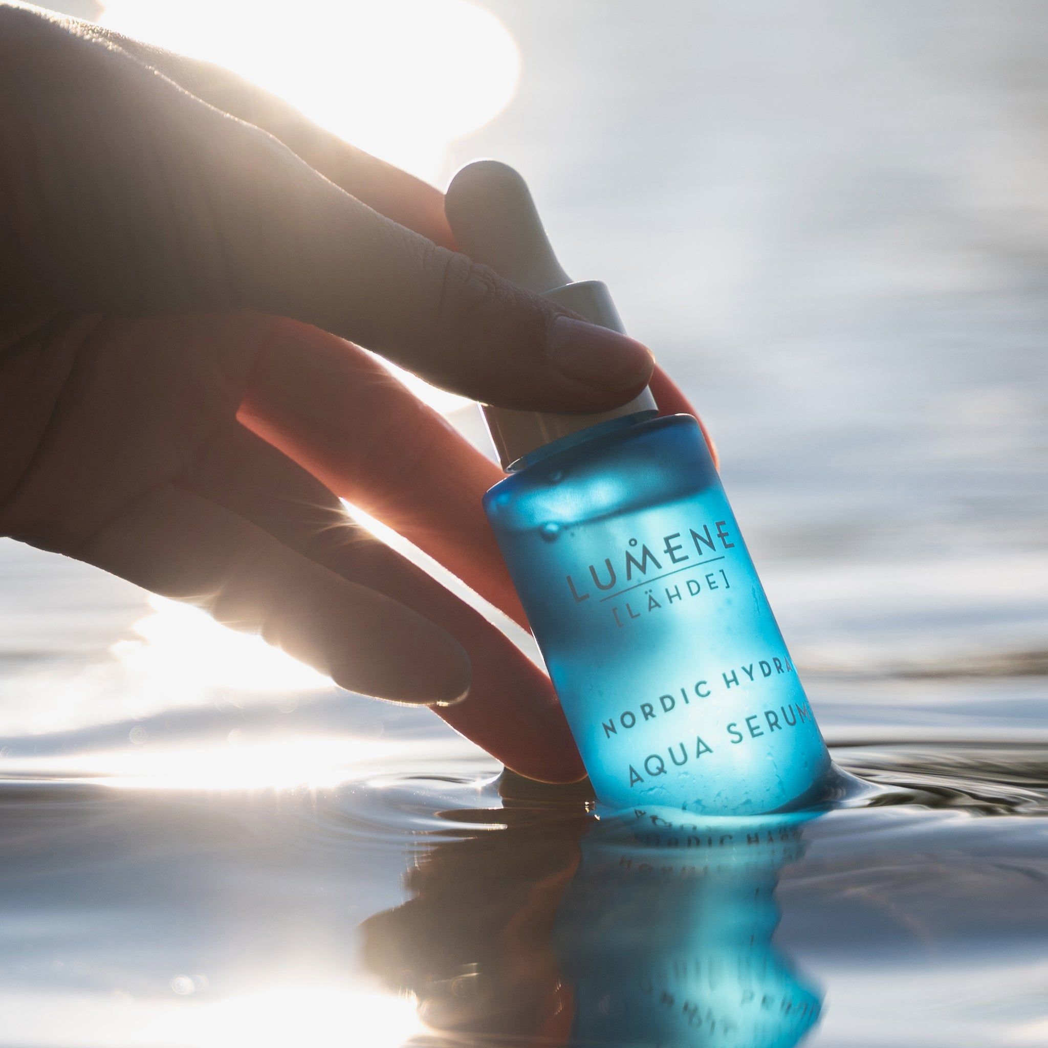 Blaue Flasche im Wasser, gehalten von einer Hand. Aufschrift: Lumene [LAHDE] Nordic Hydra Aqua Serum.