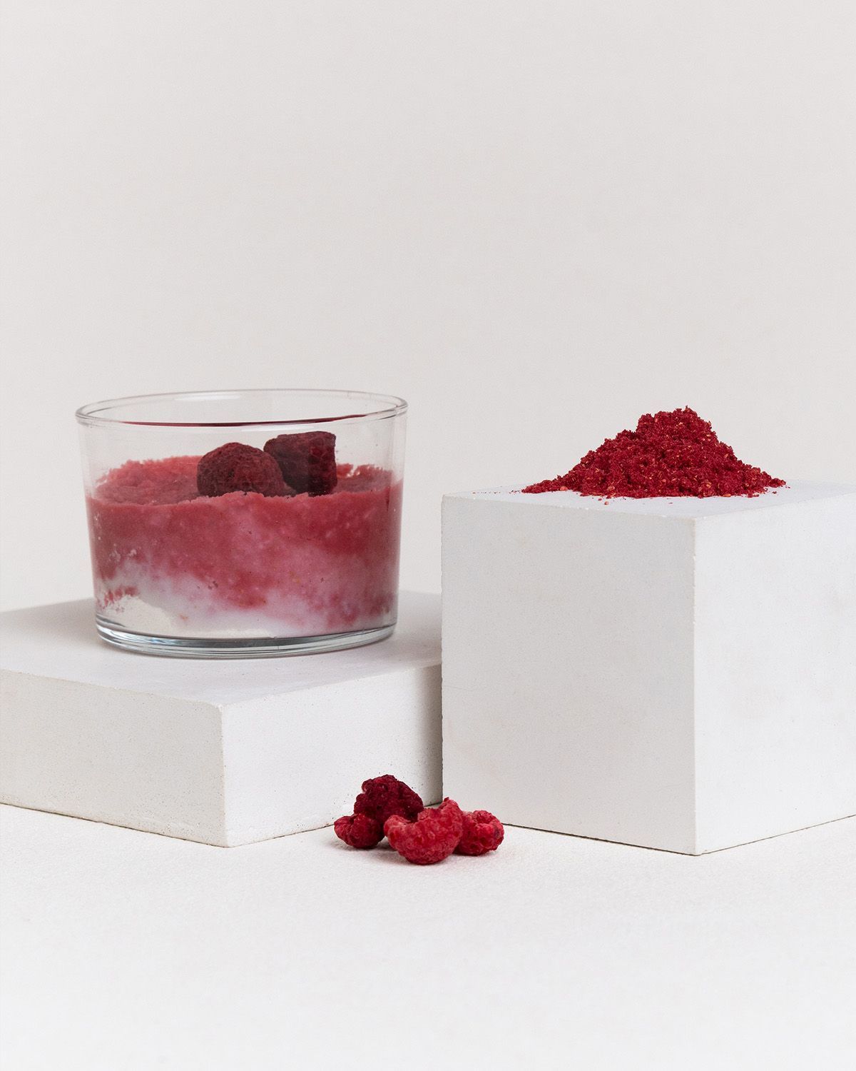 Glas mit Himbeerzubereitung, ein Würfel mit Himbeerpulver und frische Himbeeren.