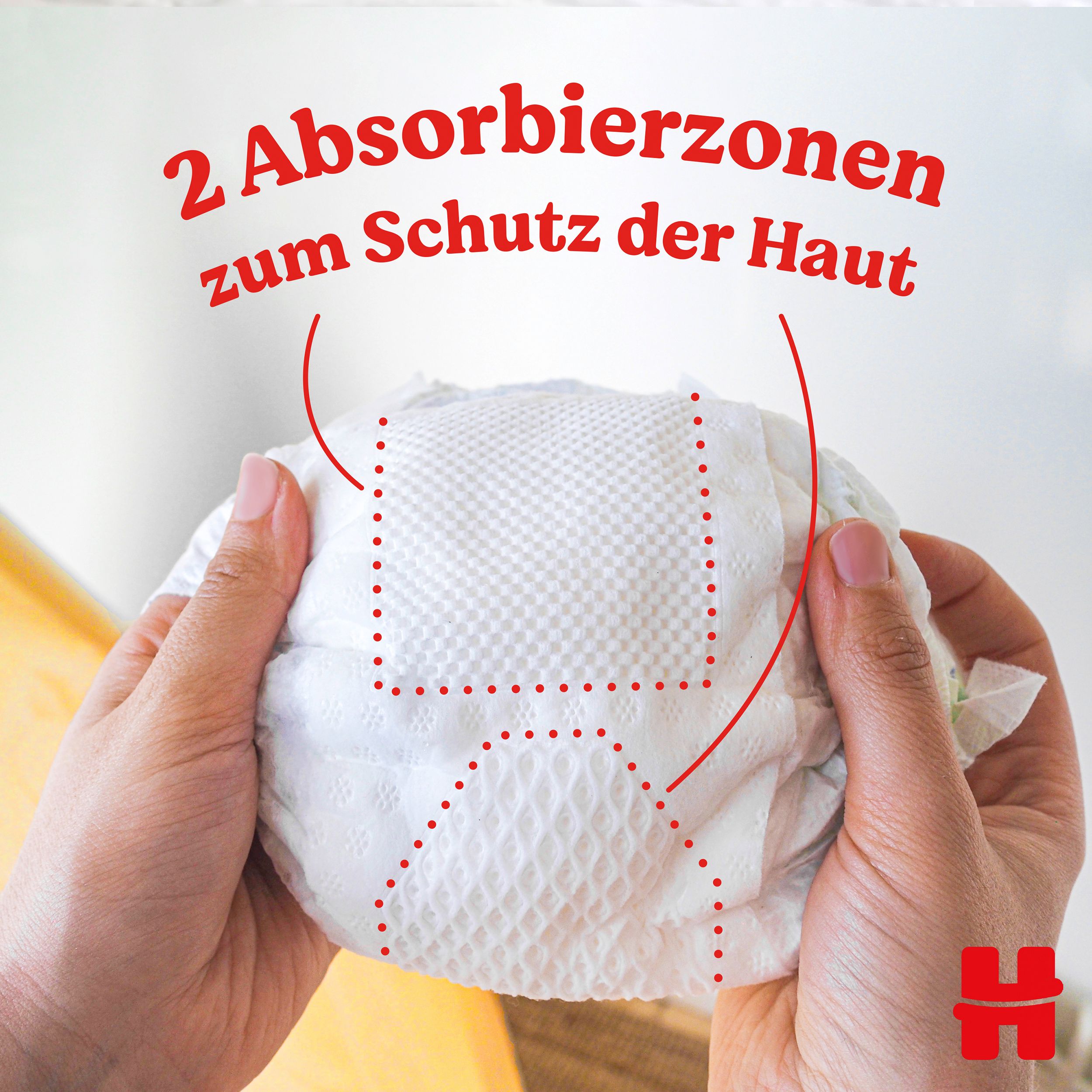 Windel mit zwei Absorptionszonen. Hände halten die Windel. Rote Linien markieren die Zonen. Logo 'H' unten rechts.