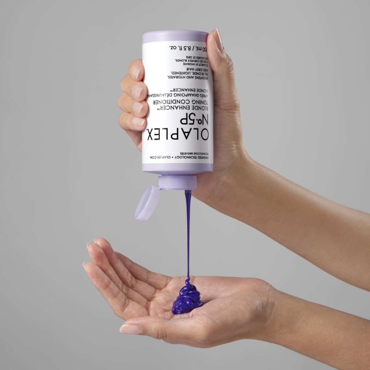 Hände halten eine Flasche Olaplex No.5P Blonde Enhancer Toning Conditioner. Lila Flüssigkeit fließt in die Handfläche. Produktname sichtbar.