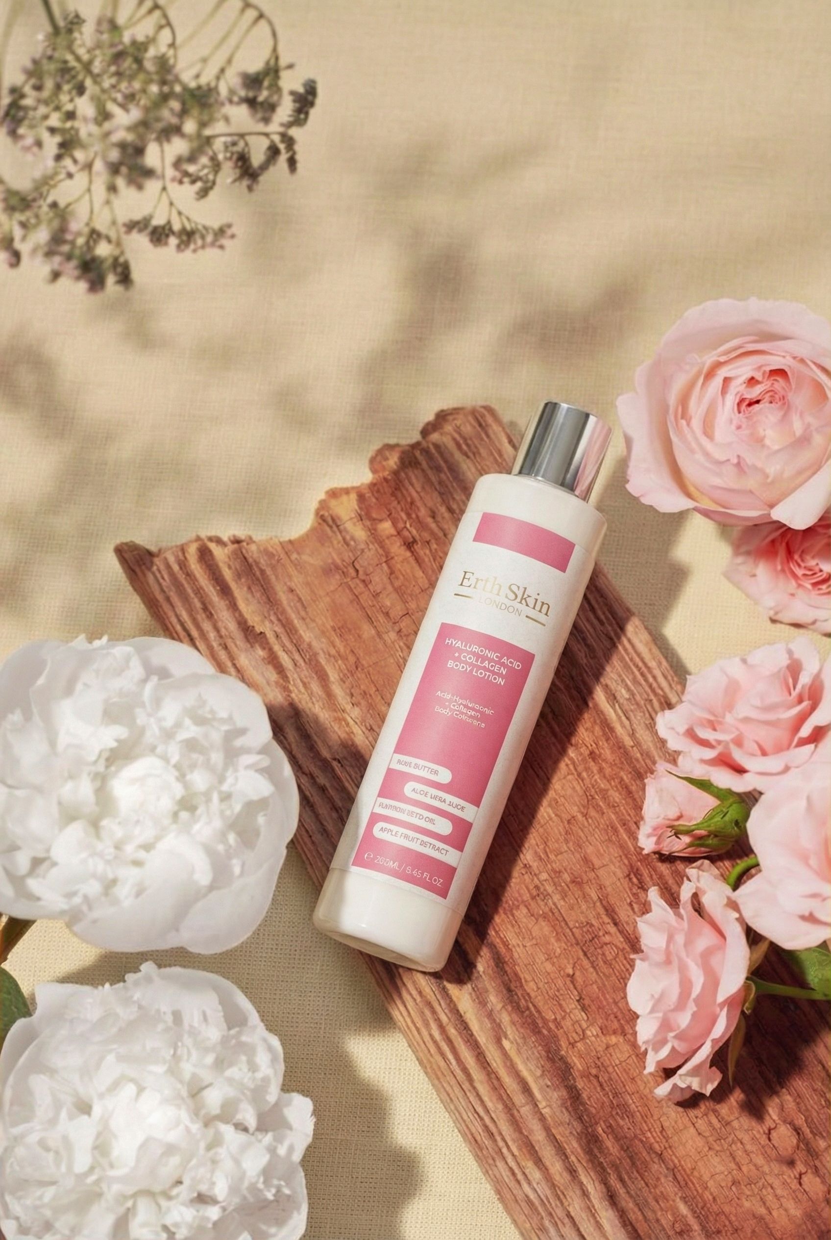 Weiße Körperlotion-Flasche mit rosa Etikett. Enthält Hyaluronsäure und Kollagen. Von ErthSkin London. Auf Holz und Blumen platziert.