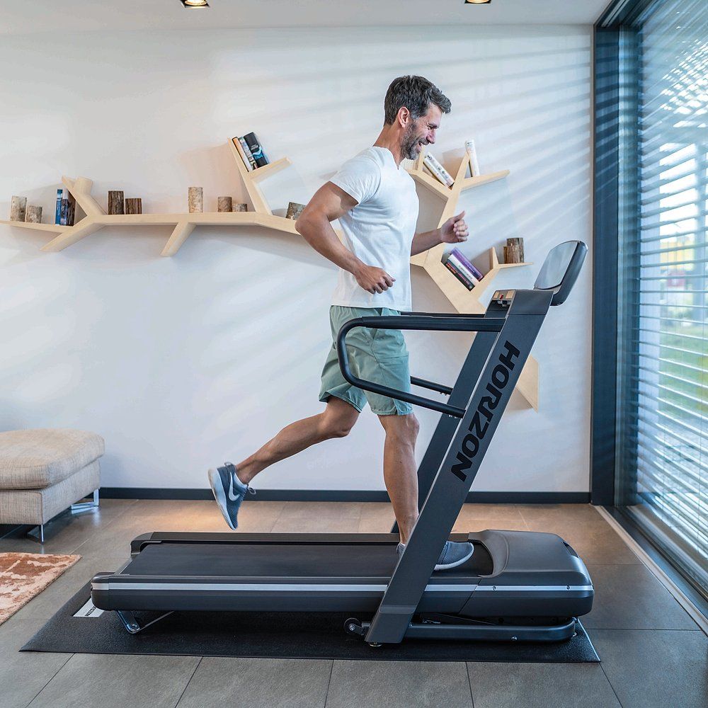 Mann läuft auf einem Laufband. Laufband mit Digitalanzeige. Marke: HORIZON. Modell: Omega Z. Umgebung: Wohnzimmer.