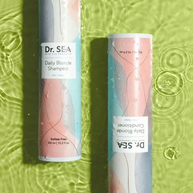 Zwei Flaschen Dr. SEA Daily Blonde Shampoo und Conditioner. Auf Wasser Hintergrund. Beide zylindrisch mit lila Deckel.