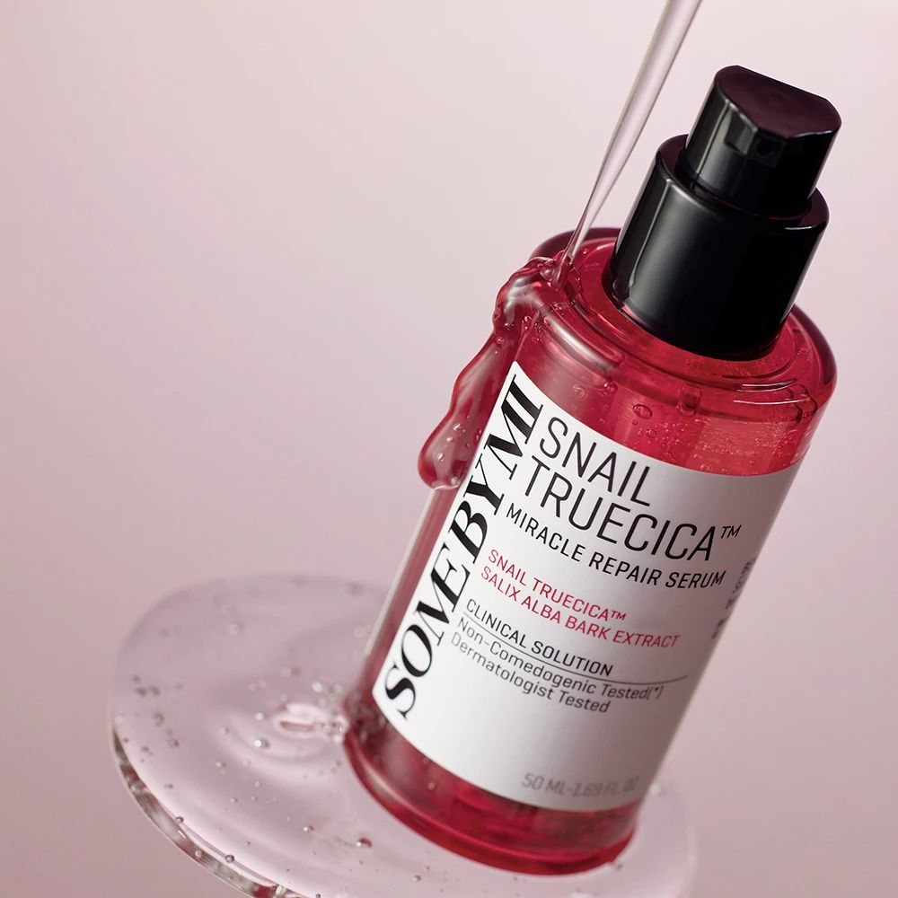 Rotes Serumfläschchen mit schwarzem Pumpverschluss. Produktname und Inhaltsstoffe auf dem Etikett. Flüssigkeit tropft aus dem Fläschchen.